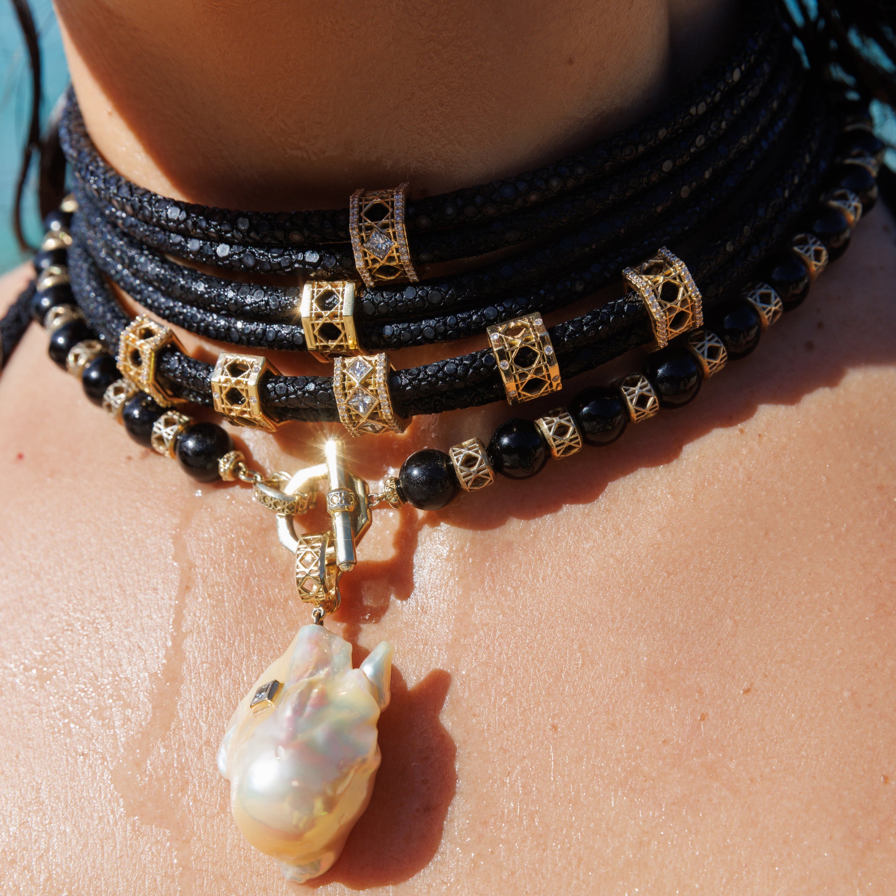 MoAnA LUU Doudou Abyss stingray leather chokers layered with Yva onyx bead necklace and Doudou Abyss south sea baroque pearl amulet in 18K yellow gold, featuring sculptural woven details inspired by Caribbean fish traps.