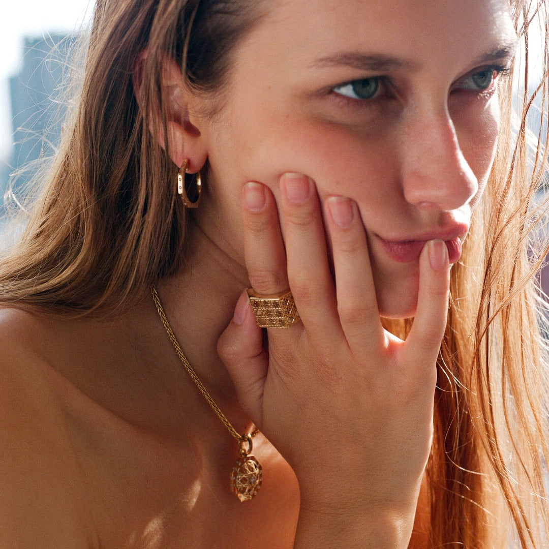 MoAnA LUU fine jewelry worn on model, featuring Ti hoop earrings and Doudou wide ring and pendant in 18K yellow gold  inspired by Caribbean fish traps.