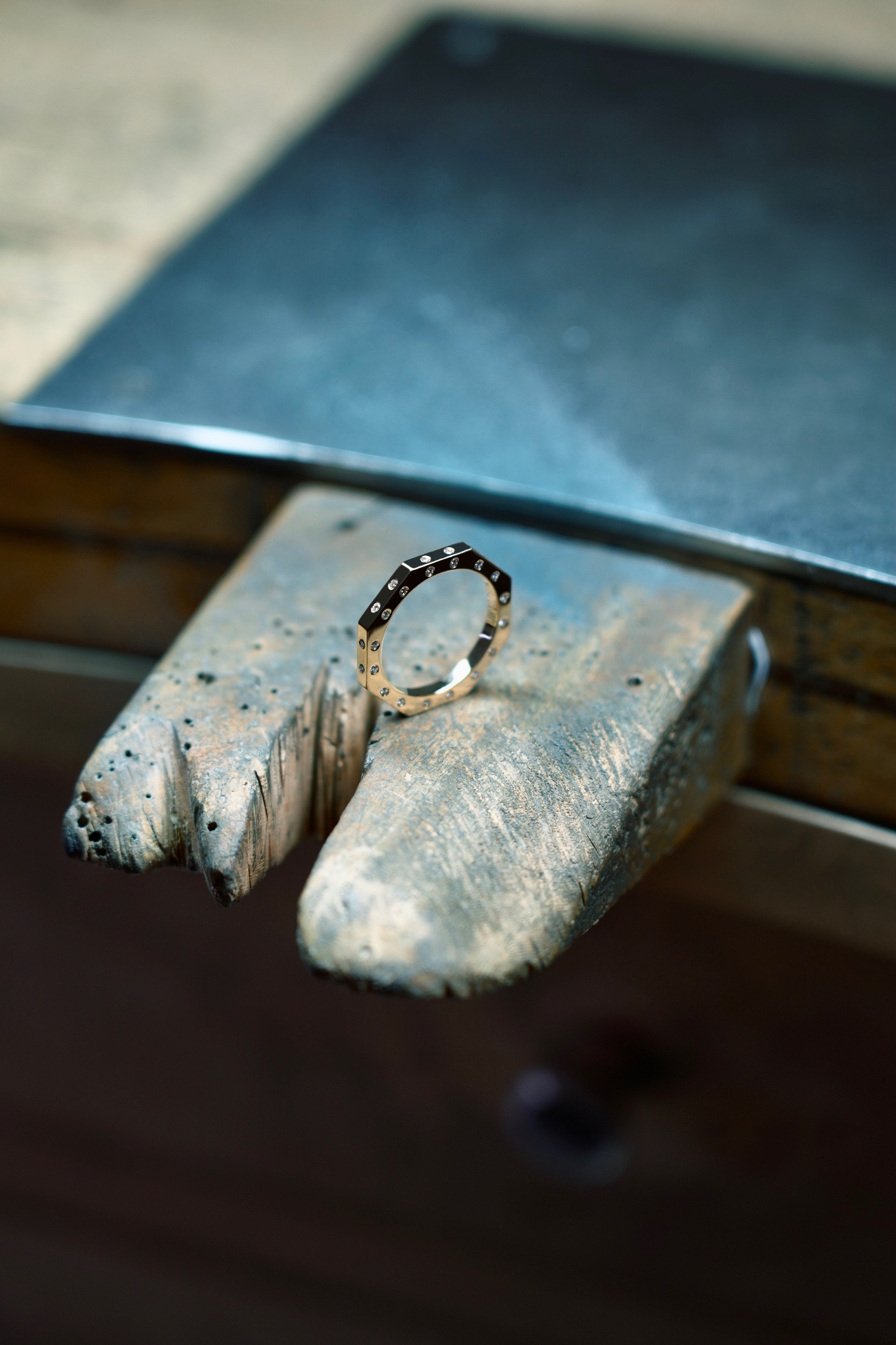 MoAnA LUU Ti ring in 18K yellow gold, featuring burnished diamonds on three sides and octogonal shape. Shown on workshop bench. 